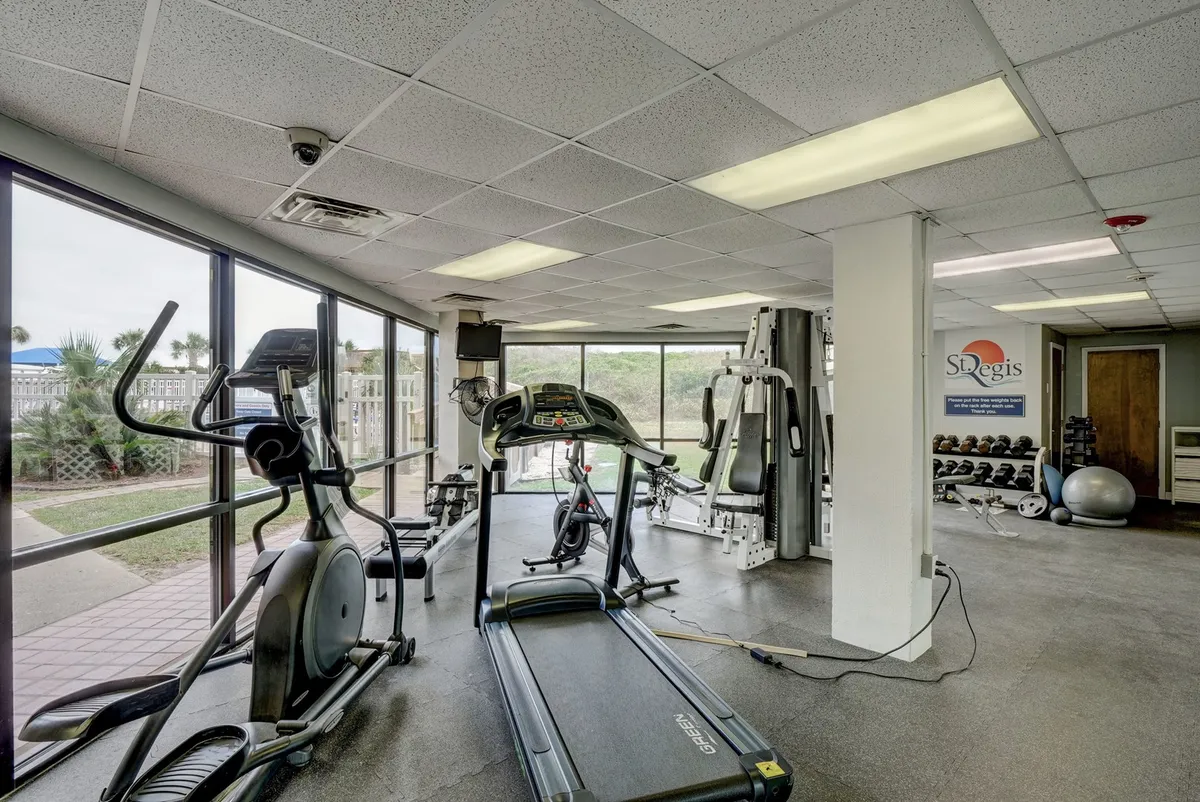 A modern fitness center featuring a treadmill, elliptical machine, and weight training equipment. The large windows provide ample natural light and views outside, creating an energetic and motivational environment for workouts.