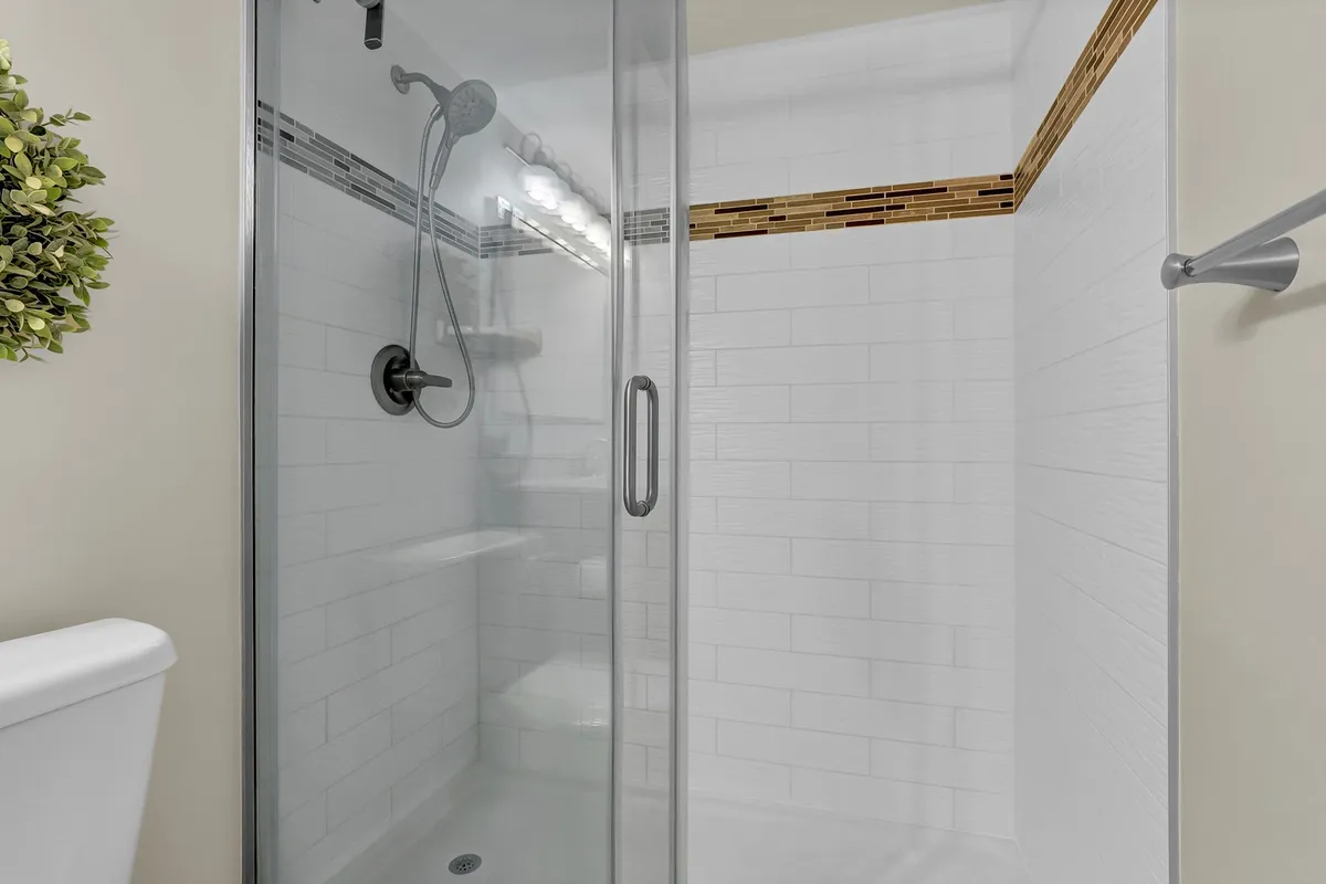 A modern bathroom with a glass shower enclosure, sleek showerhead, decorative tile accent, and a touch of greenery from a potted plant. The space is inviting and fresh, perfect for relaxing after a sunny day at the coast.