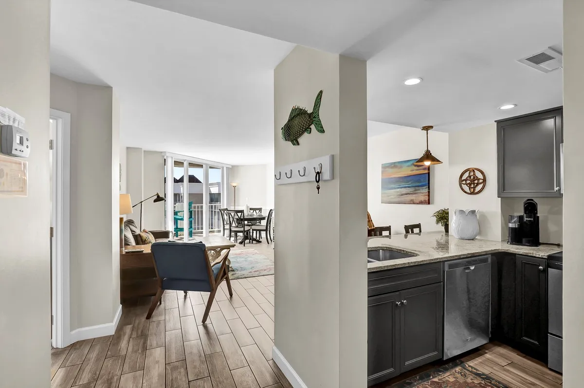 An inviting open-plan area showcasing a kitchen island, a connected dining area, and a living room with large windows flooding the space with natural light. Decorative fish motifs evoke a coastal vibe, while the setup encourages relaxation and social interaction.