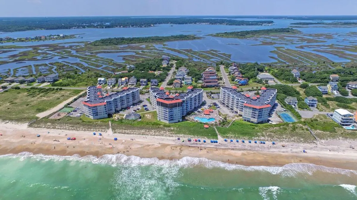 A vibrant resort scene featuring beachfront buildings, a swimming pool with sparkling water, and the ocean waves just steps away. Colorful umbrellas dot the poolside, creating a lively atmosphere for families to gather, swim, and relax together.