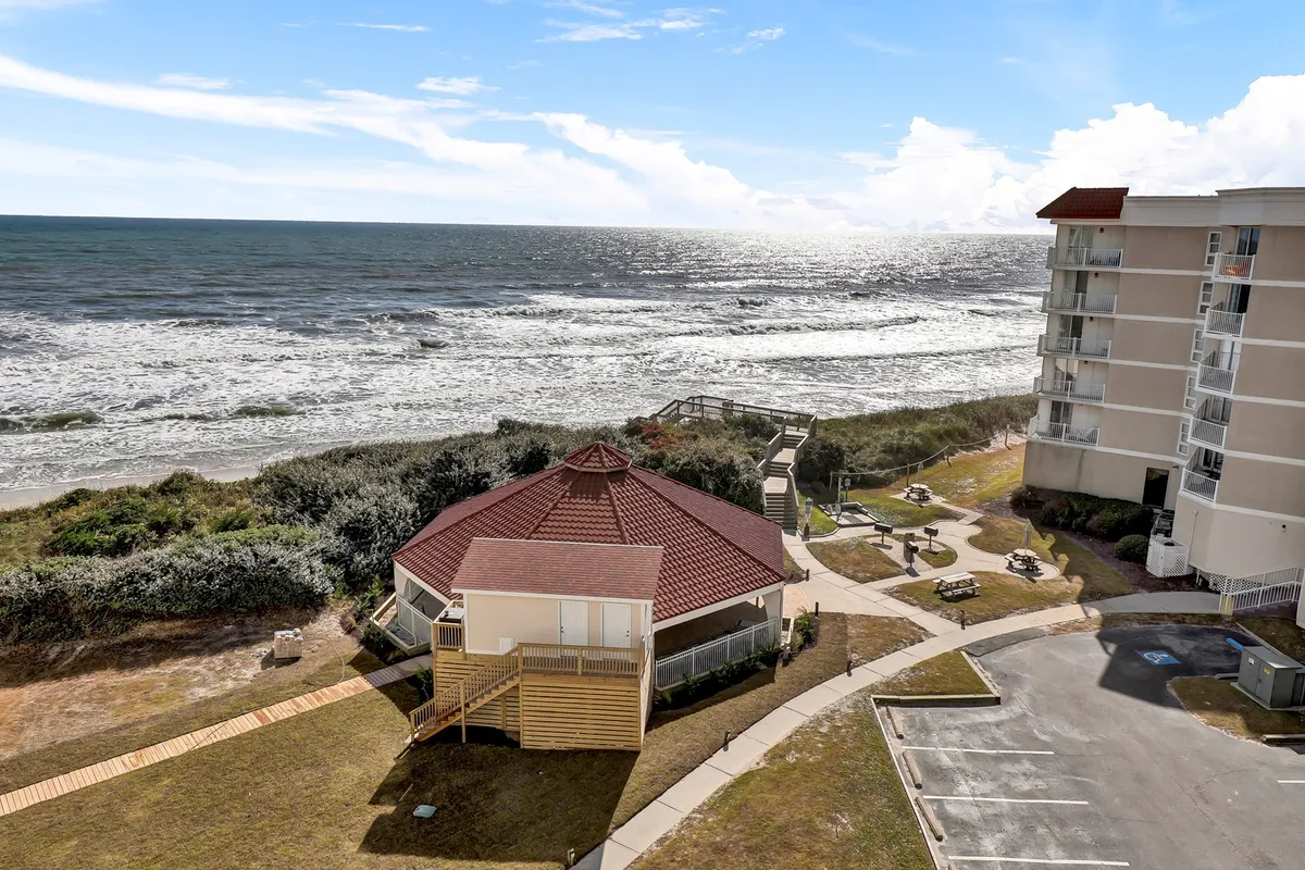 An expansive exterior shot capturing the path leading to a quiet beach, framed by a distinctive circular building and inviting seating areas. The view emphasizes the connection between the resort and the natural shoreline, ideal for romantic walks and shared moments by the sea.