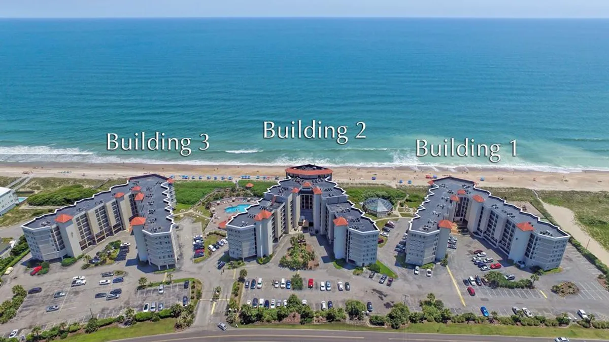 This exterior image features a shimmering swimming pool surrounded by sun loungers, with buildings arranged to maximize ocean views in the background. The tranquil pool area invites relaxation and togetherness, while the proximity to the beach enhances the sense of a coastal retreat.